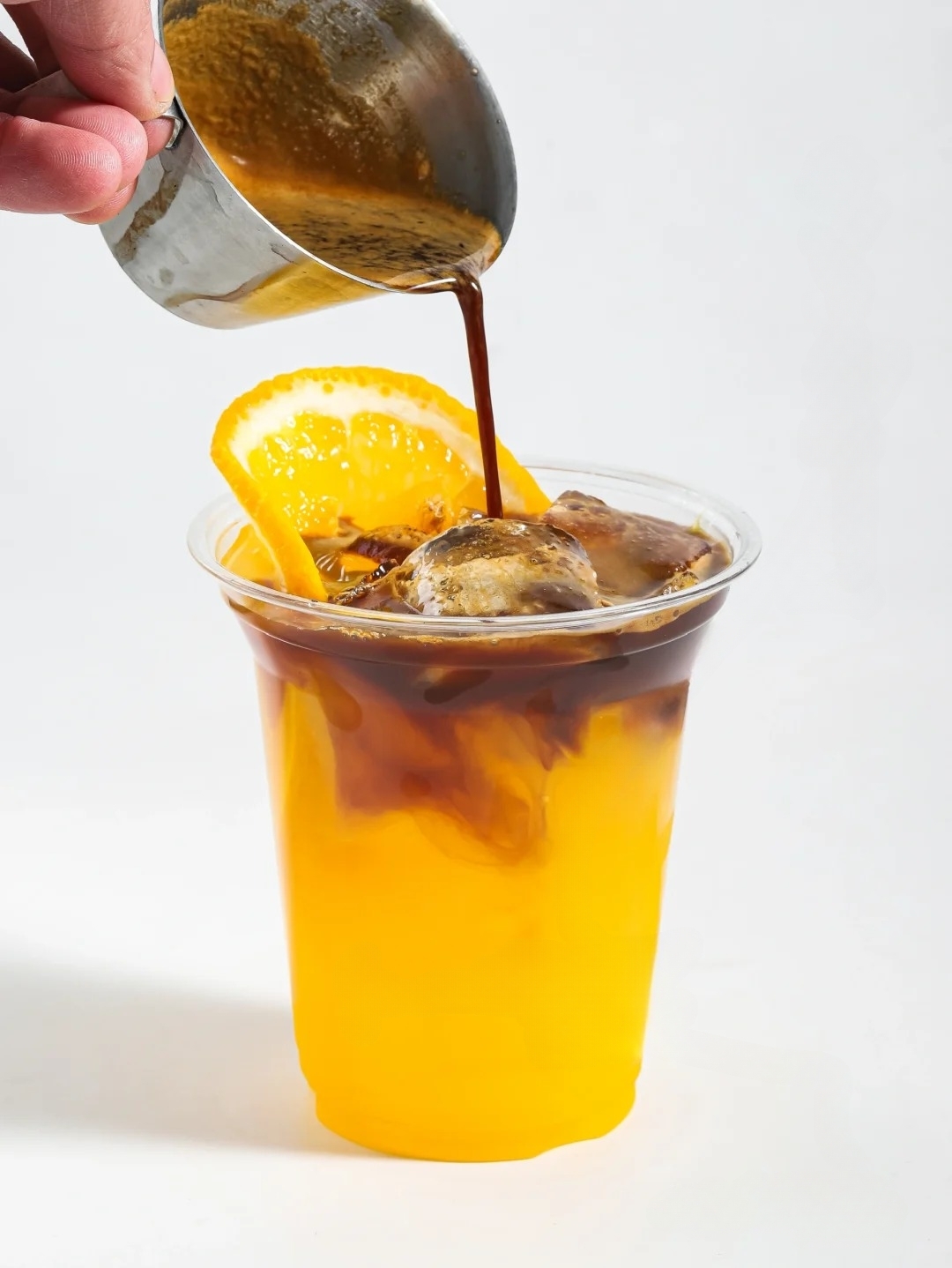 A tall glass filled with ice cold brew coffee topped with a sliced orange and orange peel garnish.