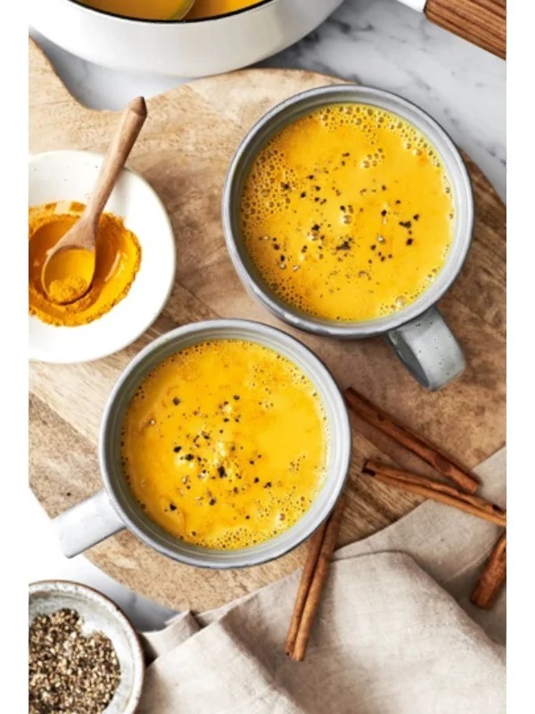 A mug of frothy turmeric golden milk latte with a cinnamon stick on a wooden table.