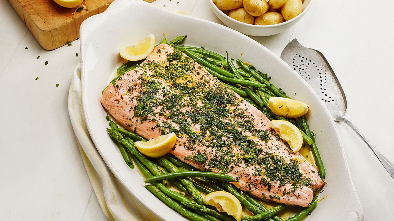 A white plate with a baked salmon fillet topped with lemon slices and fresh asparagus spears.