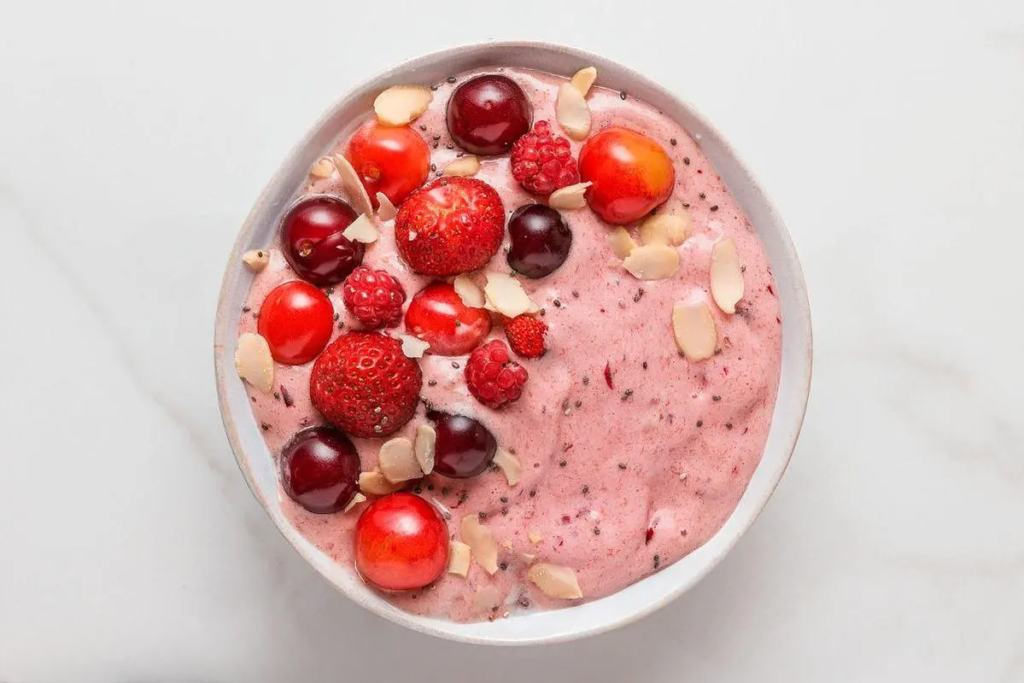 A glass filled with a thick, pink smoothie made with mixed berries and topped with fresh berries for garnish.