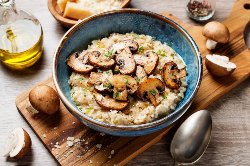 Creamy mushroom risotto topped with sliced mushrooms and fresh parsley in a blue ceramic bowl on a wooden cutting board.