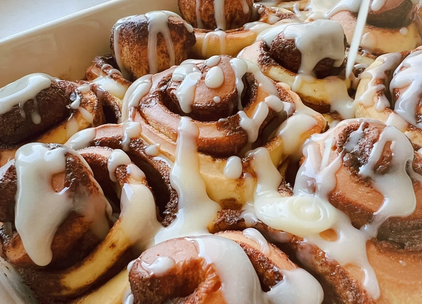 A plate overflowing with fluffy, golden brown cinnamon rolls drizzled with rich cream cheese icing.