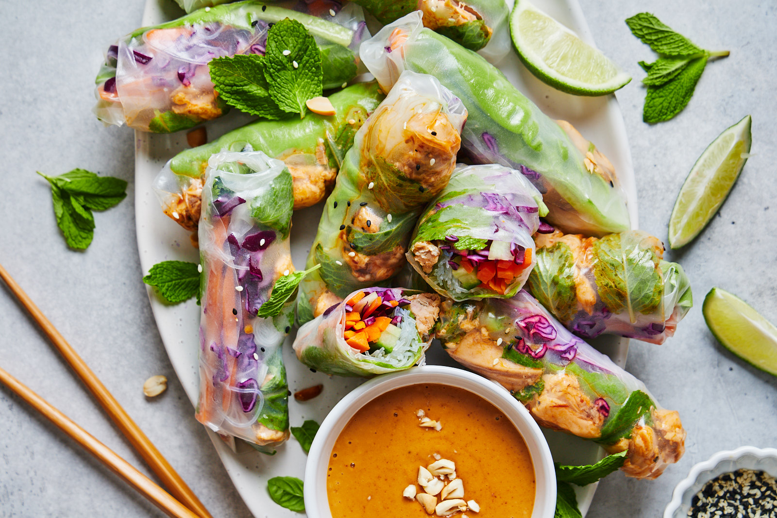 A plate of fresh spring rolls with colorful vegetables wrapped in rice paper alongside a bowl of peanut dipping sauce.