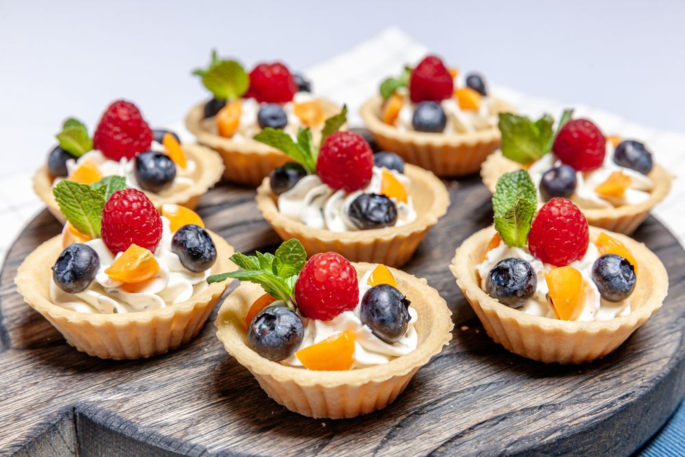 A delicious mini fruit tart with creamy filling and fresh berries, beautifully presented on a wooden plate. Yum! 🍓🥧🍇