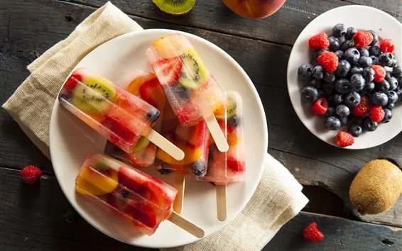 A plate of colorful homemade popsicles made from various fruits next to a plate of fresh berries.