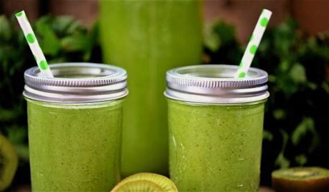 A mason jar filled with a green smoothie made with kale, spinach, and fruits, garnished with a straw.