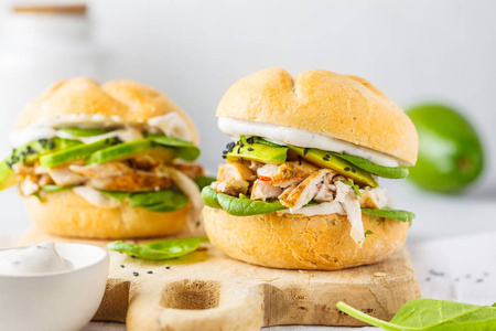 A close-up photo of a halved grilled chicken and avocado wrap on a wooden cutting board. The wrap is filled with sliced grilled chicken breast, avocado slices, lettuce, tomato, and cheese. It is wrapped in a whole wheat tortilla and cut in half to reveal the filling.