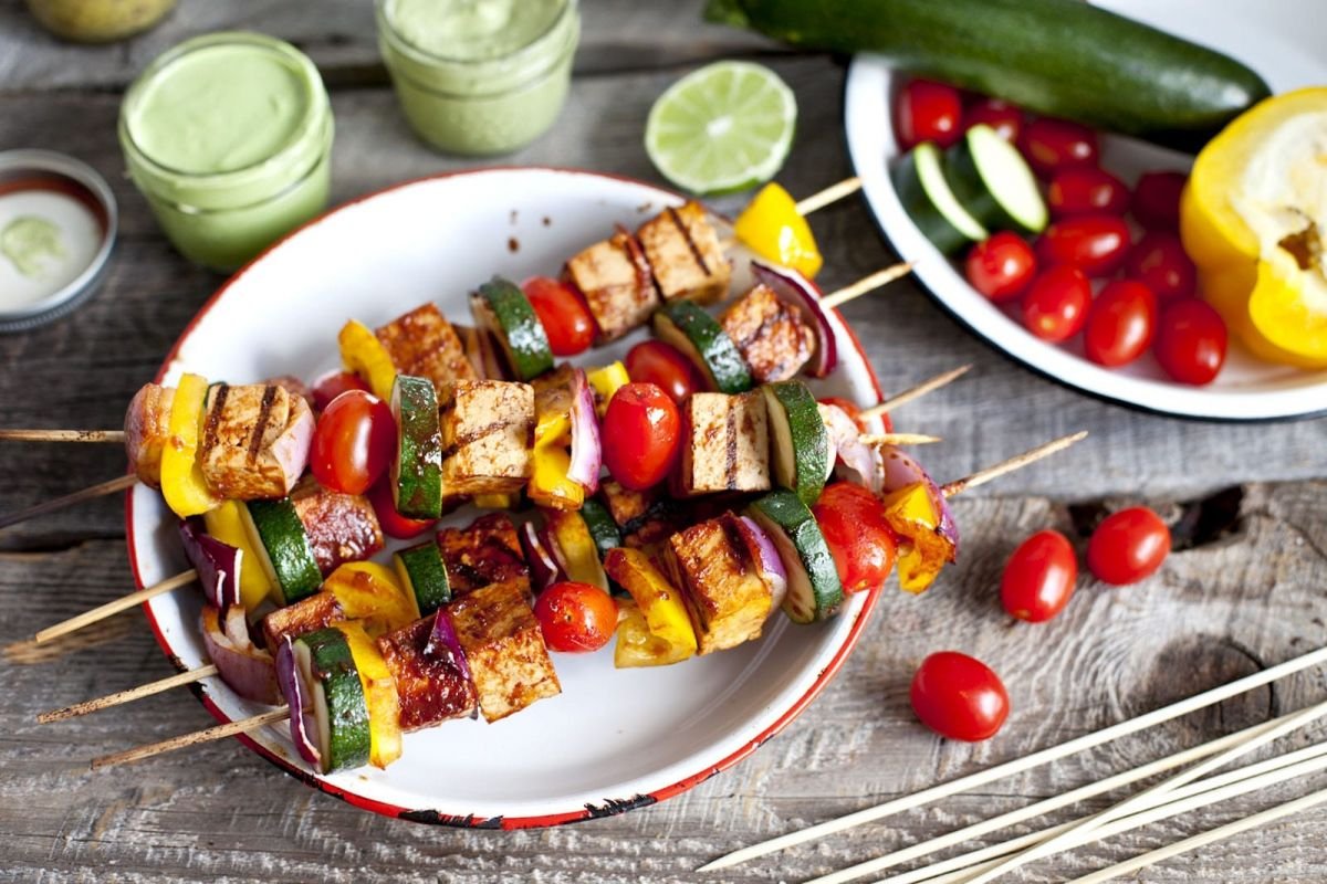 A plate of colorful grilled vegetable skewers with a side of tzatziki sauce.