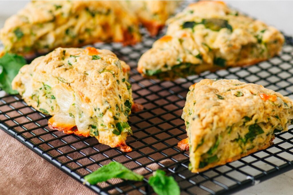 A close-up photo of a group of golden brown savory scones with fresh herbs on a cooling rack.