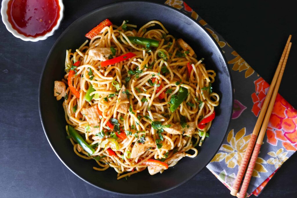 A black bowl filled with rice noodles, vegetables, and peanuts in a peanut sauce.