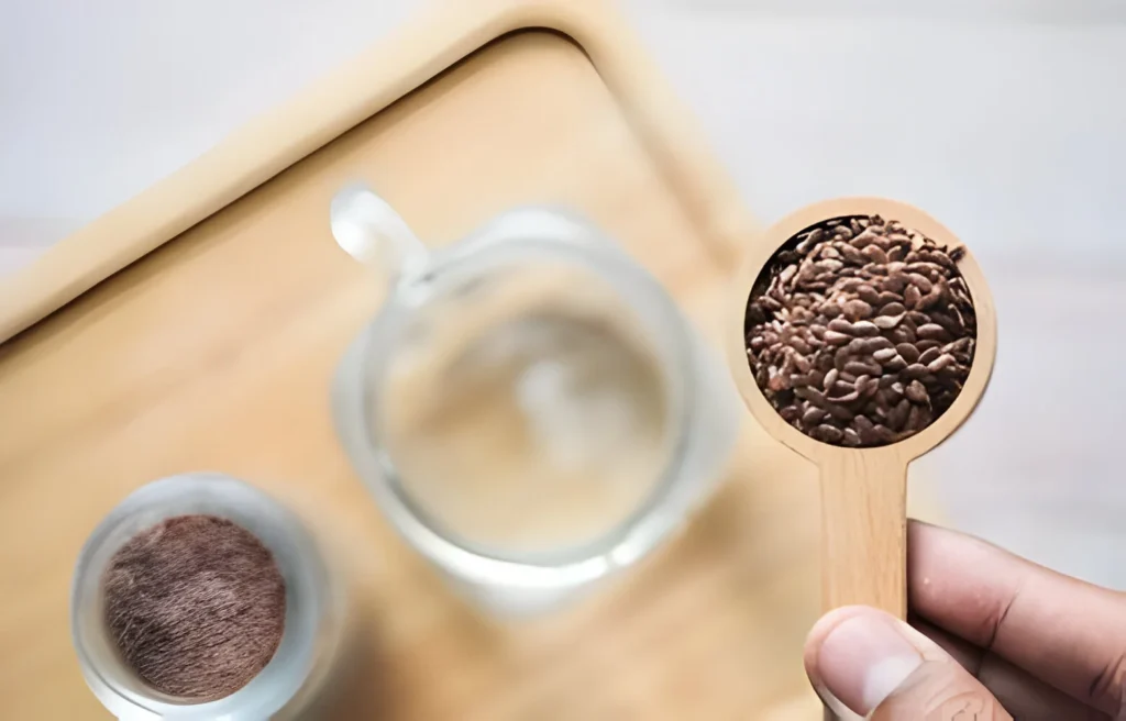 A wooden spoon filled with flax seeds held above a glass of water.