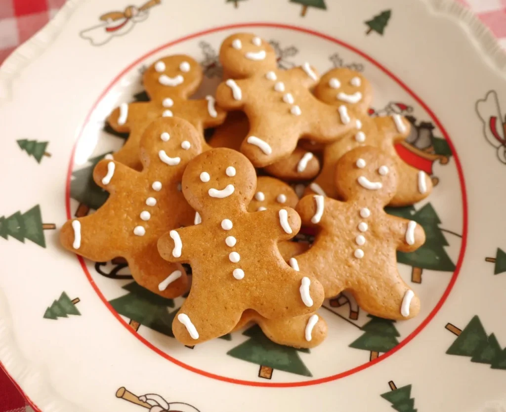 A plate of gingerbread cookies decorated with red and white frosting, in the shape of Christmas trees