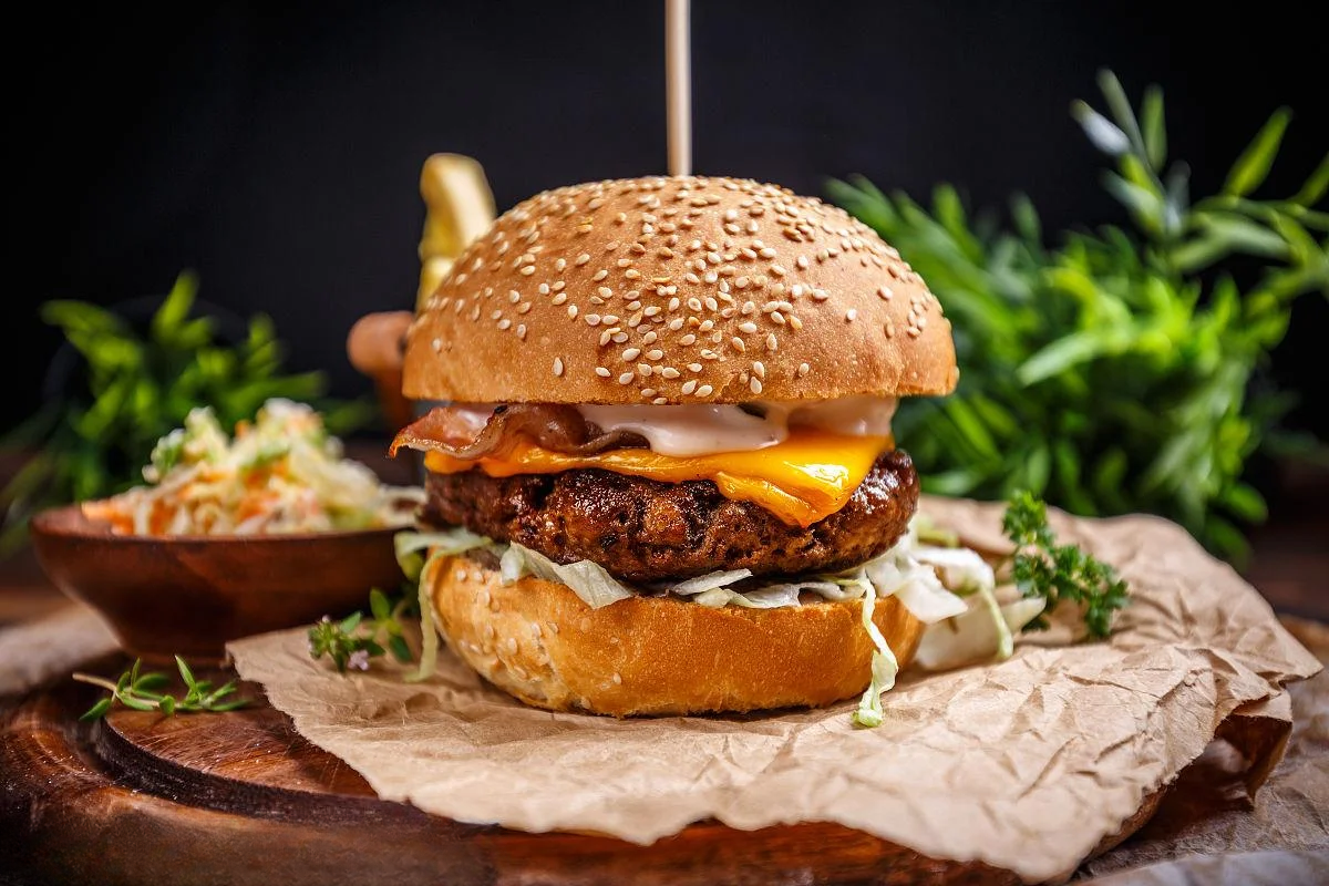 Gourmet grilled burger with melted cheese, bacon, and coleslaw on a sesame seed bun