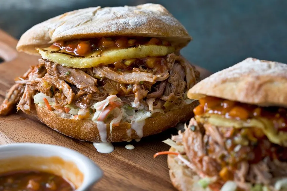 Two pulled pork sandwiches on a wooden cutting board with a side of coleslaw in a small bowl.