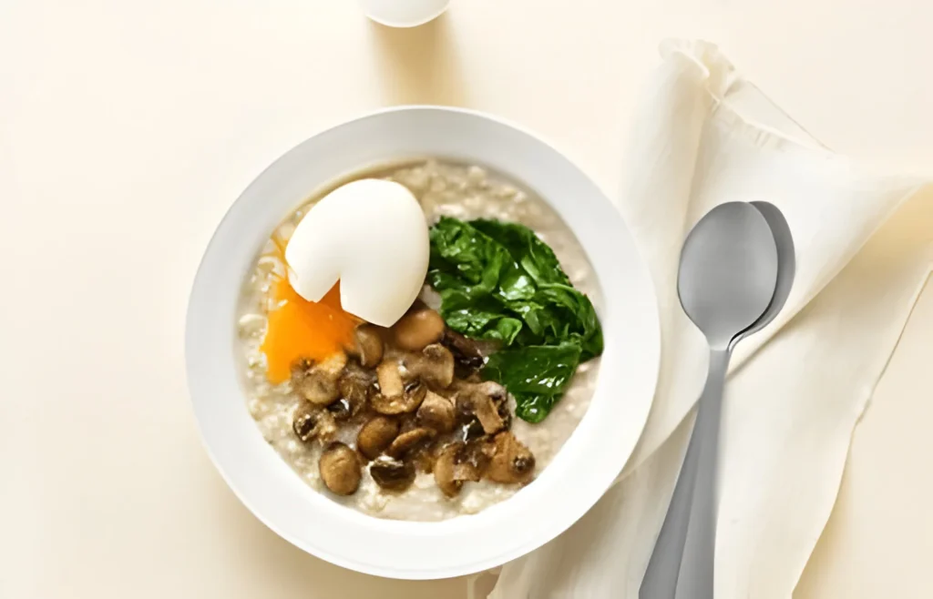 Bowl of spinach oatmeal topped with sautéed mushrooms and a poached egg, served on a white tablecloth with a spoon