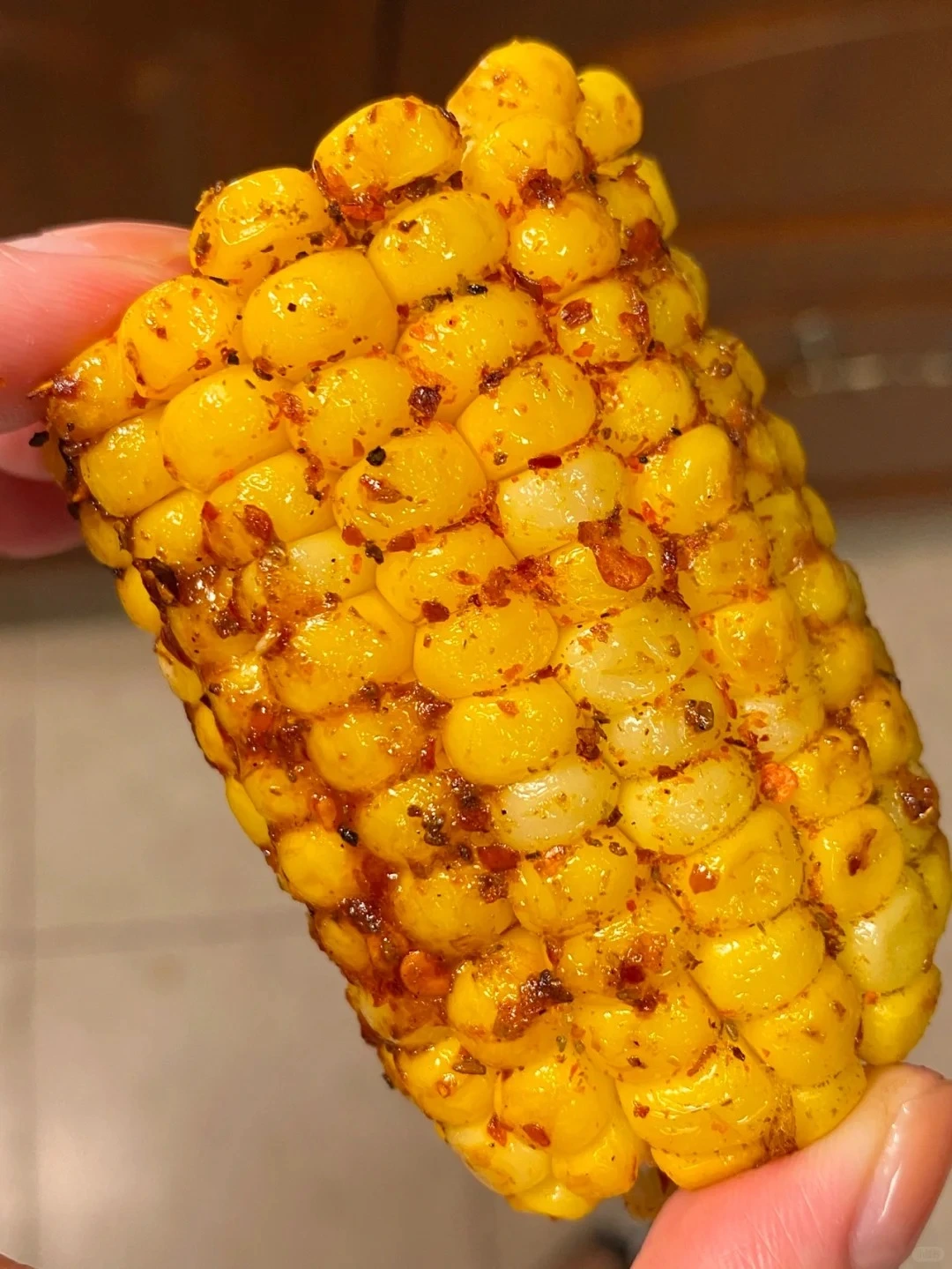 A close-up view of a hand holding a vibrant yellow ear of grilled corn on the cob. The plump, juicy kernels glisten with a luscious coating of melted butter, their charred edges hinting at a smoky, caramelized flavor. The corn, a delectable summertime treat, beckons with its irresistible aroma and promises a burst of sweet, tender satisfaction.