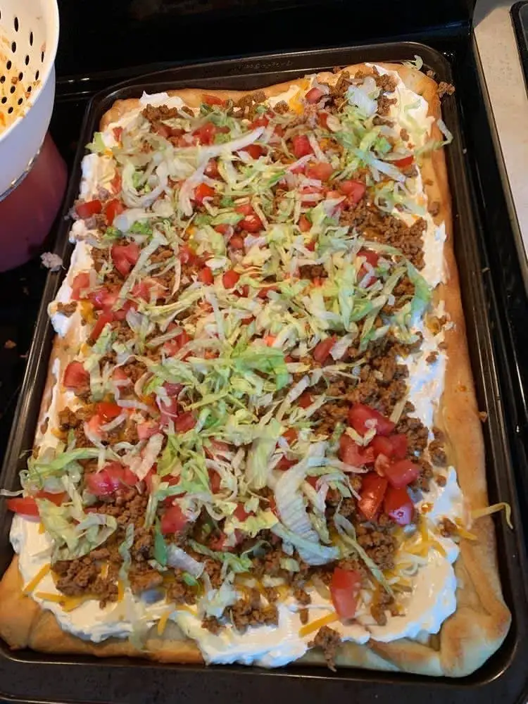 A delicious homemade taco pizza topped with seasoned ground beef, shredded lettuce, diced tomatoes, and sour cream on a crispy crust.