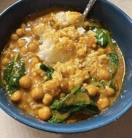 A bowl of steaming chickpea and spinach curry with a spoon, showcasing a creamy golden sauce, plump chickpeas, and vibrant green spinach leaves