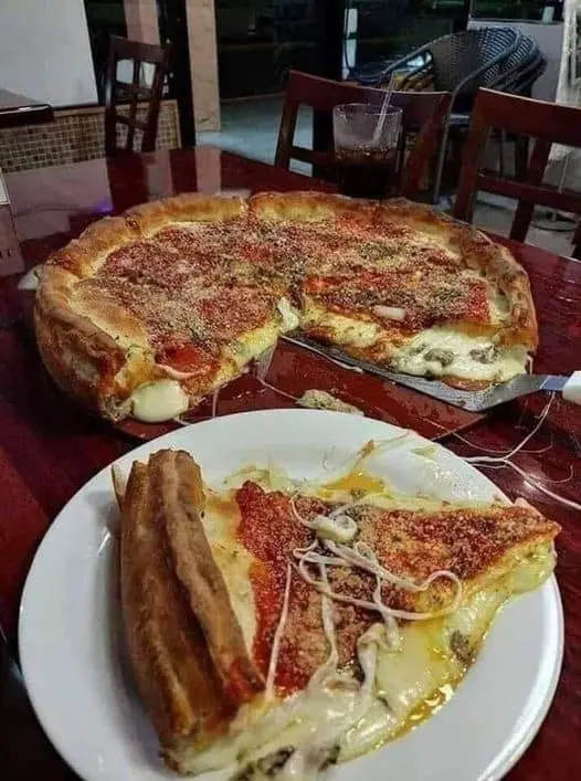 Freshly baked Chicago-style deep dish pizza with thick crust, melted cheese, and tomato sauce, served on a red table with a slice on a plate