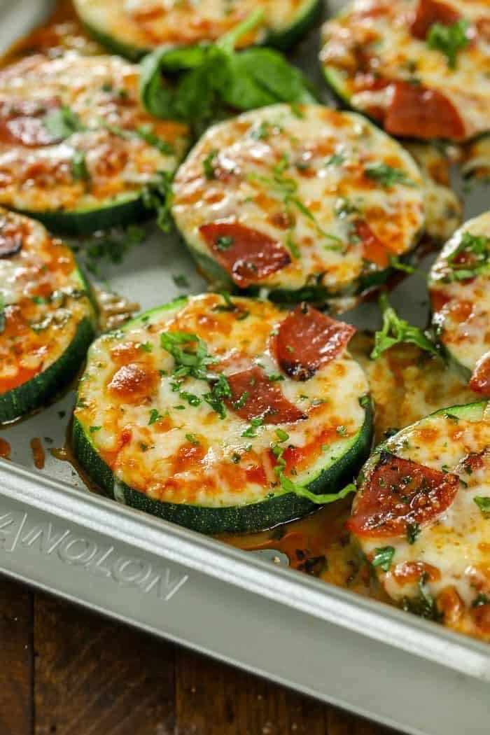 Close-up of baked zucchini slices topped with melted cheese, pepperoni, and herbs on a baking sheet