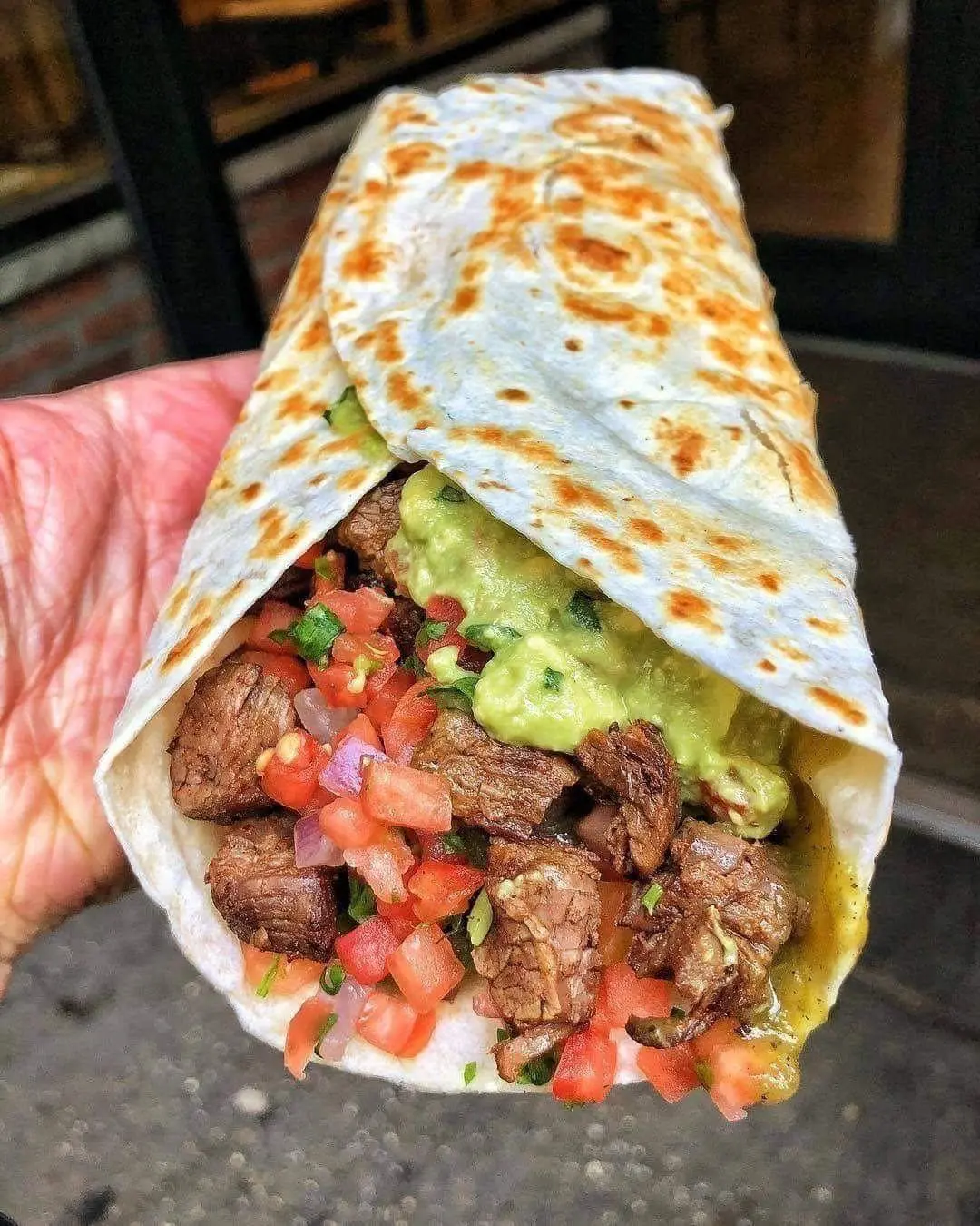 Hand holding a freshly made loaded steak quesadilla filled with seasoned beef, diced tomatoes, and creamy guacamole.