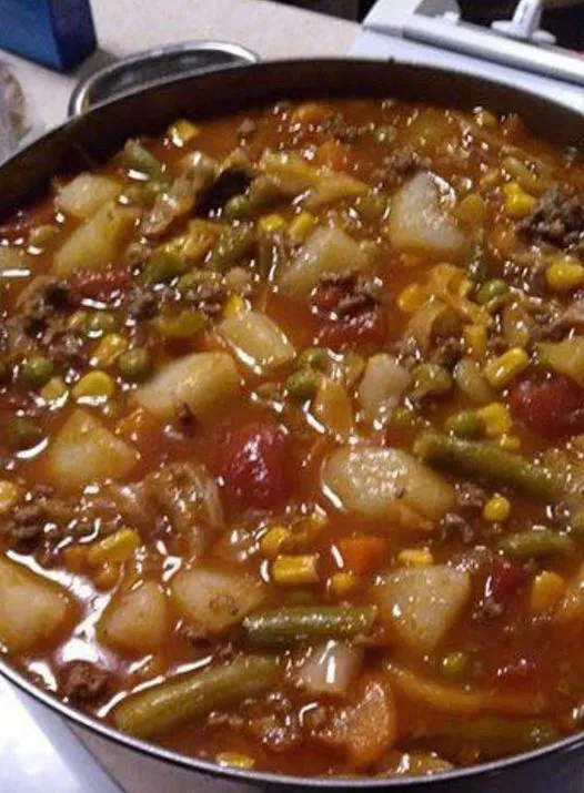 Steaming pot of homemade vegetable beef soup with chunks of potato, ground beef, corn, and green beans in a rich tomato broth