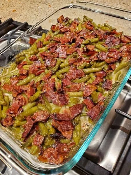 A baking dish filled with crack green beans topped with crispy bacon pieces, freshly baked and ready to serve