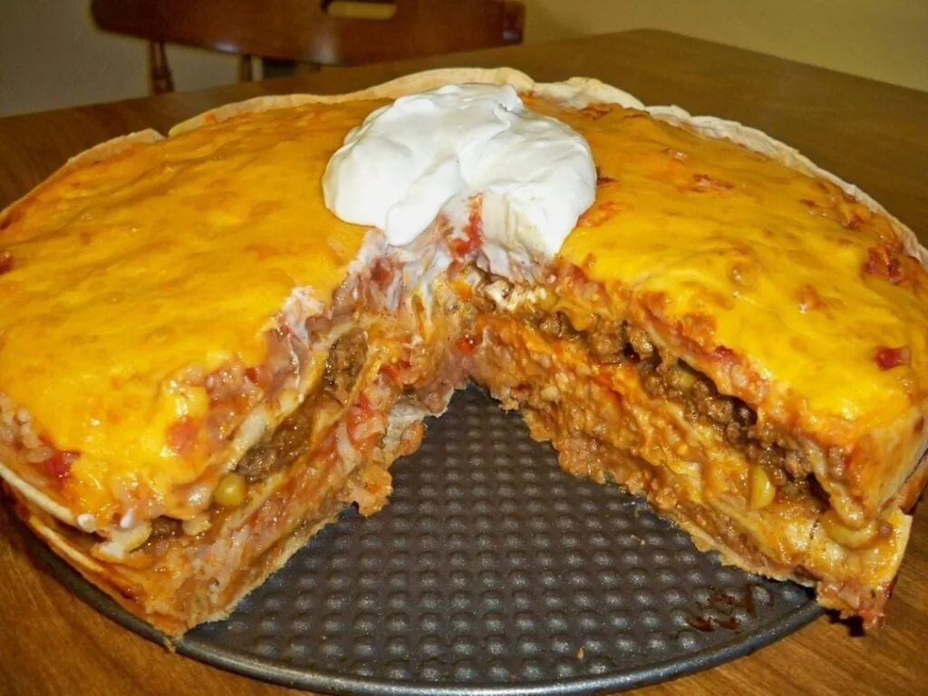 A delicious Mexican Tortilla Casserole with layers of ground beef, refried beans, corn, salsa, and melted cheddar cheese, topped with a dollop of sour cream.