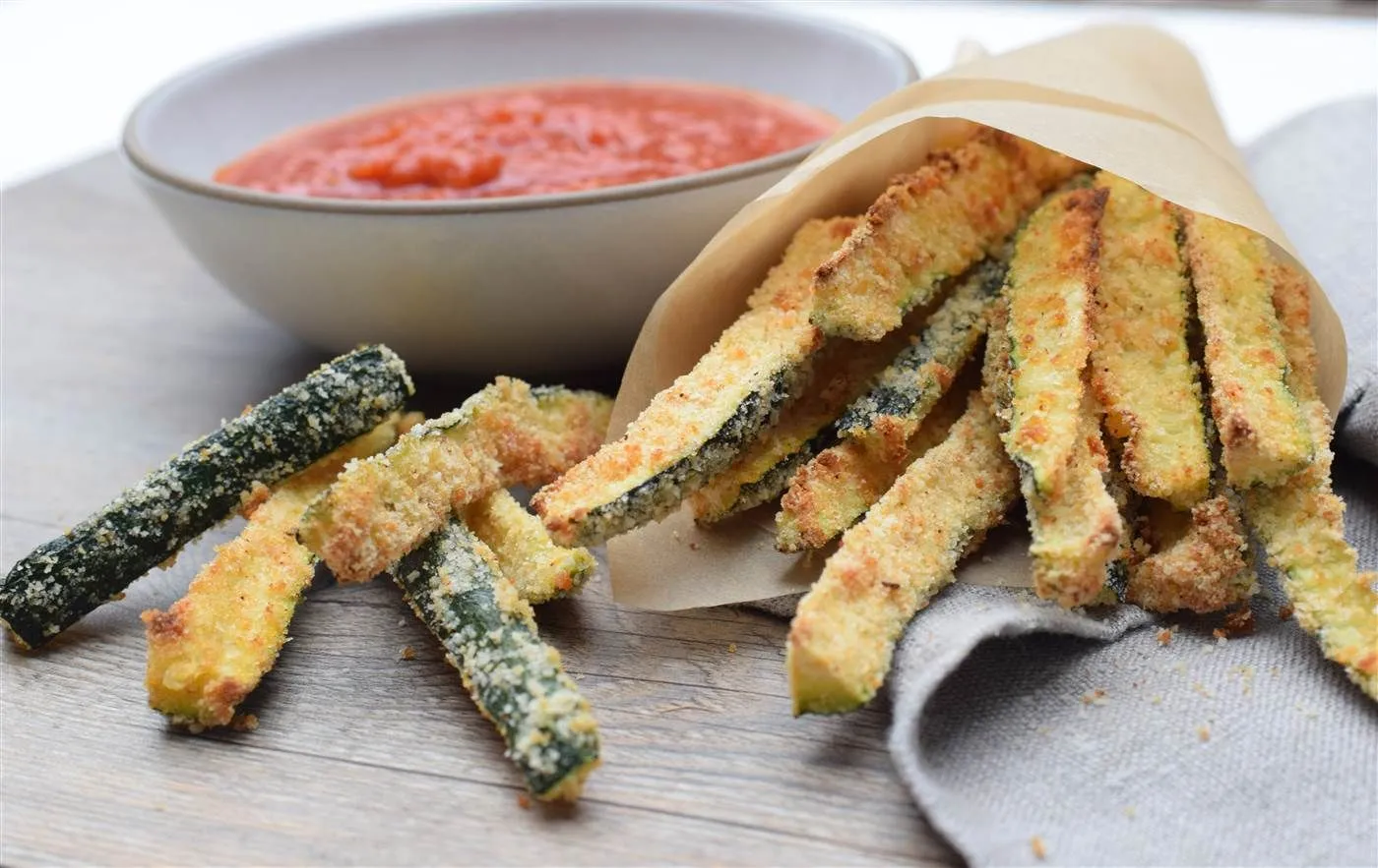 Plate of crispy baked zucchini fries with a bowl of marinara dipping sauce.