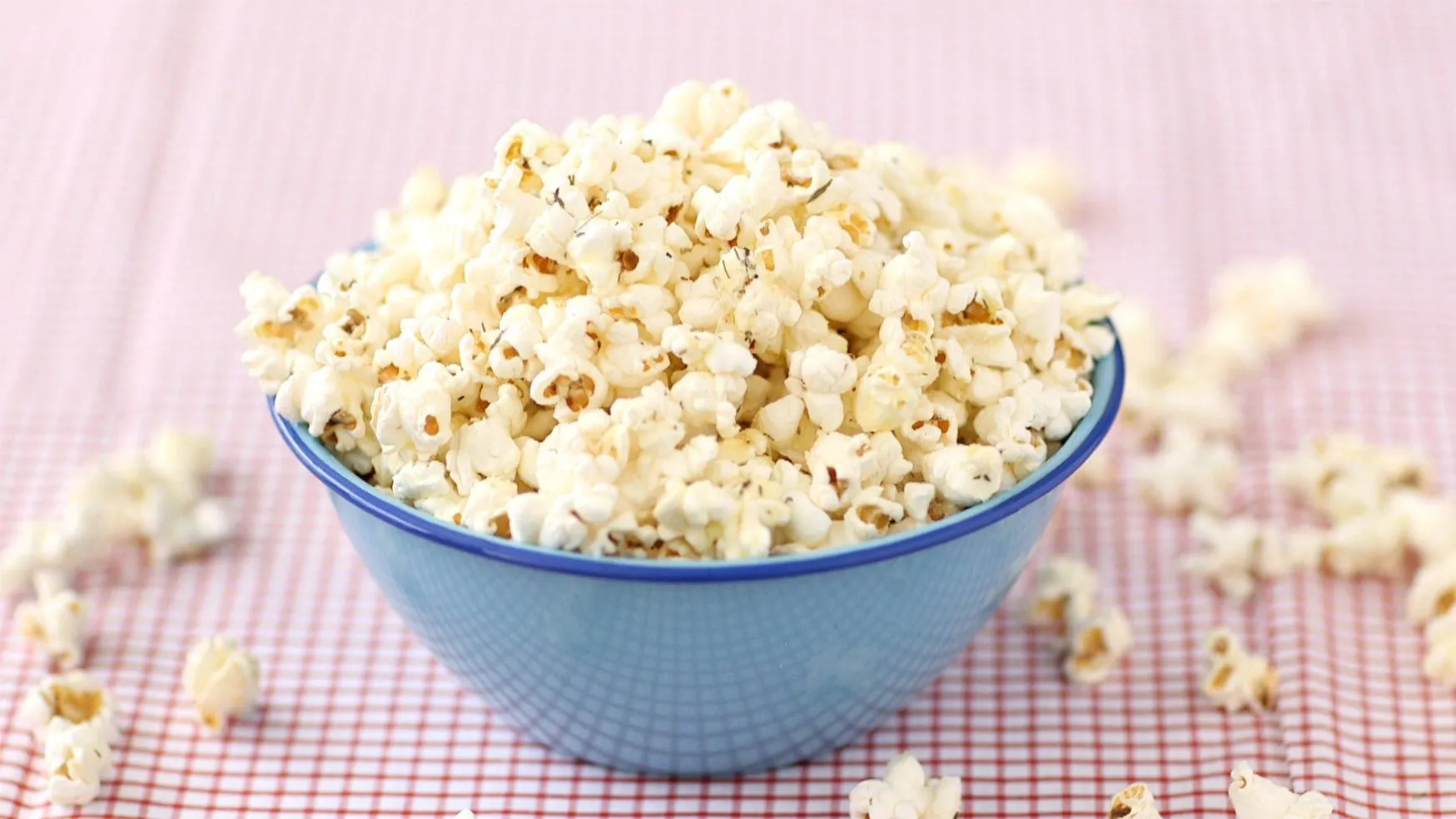 Blue bowl filled with freshly made garlic Parmesan popcorn on a red and white checkered tablecloth