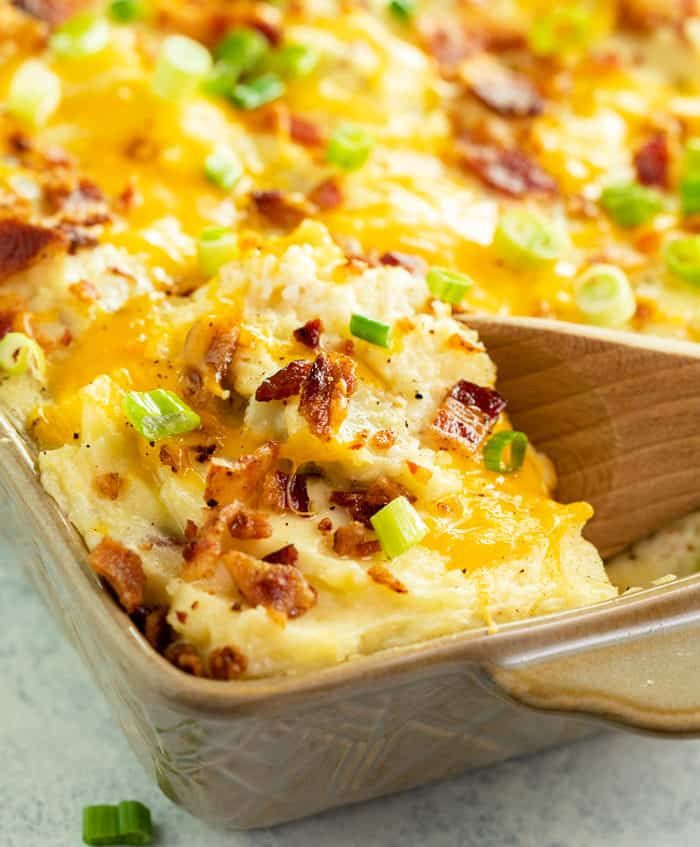 Creamy twice baked potato casserole with melted cheese and bacon bits, served in a white baking dish with a portion on a small plate