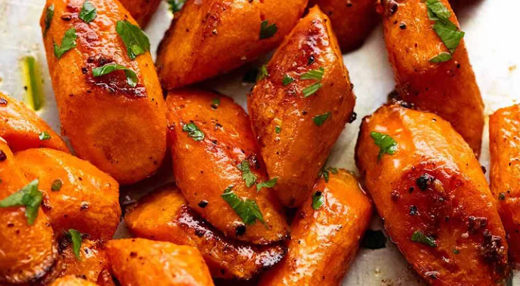 Close-up of golden-brown maple glazed roasted carrots garnished with fresh herbs