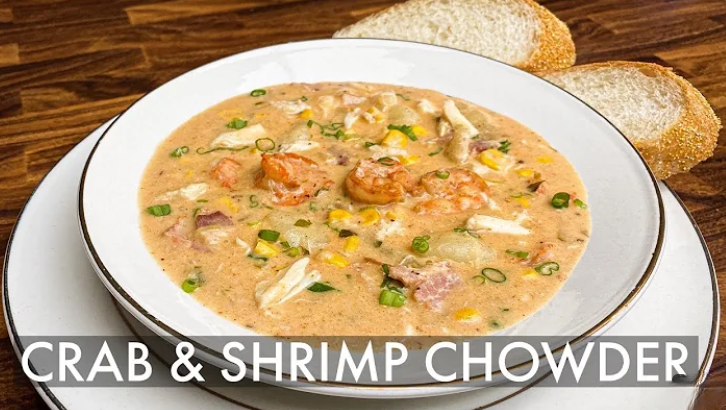 A bowl of creamy crab and shrimp chowder with corn, bacon, and green onions, served with crusty bread