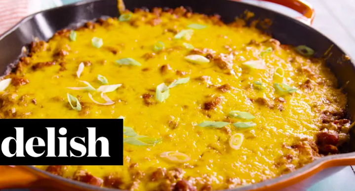 A sizzling skillet filled with hearty chili topped with a golden layer of cornbread and melted cheese, garnished with green onions.