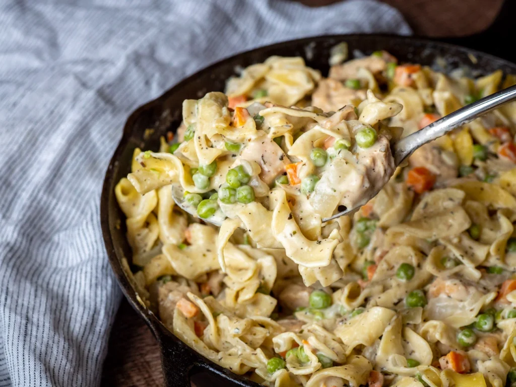 Creamy chicken pot pie noodle skillet with egg noodles, chunks of chicken, peas, and carrots in a cast iron pan