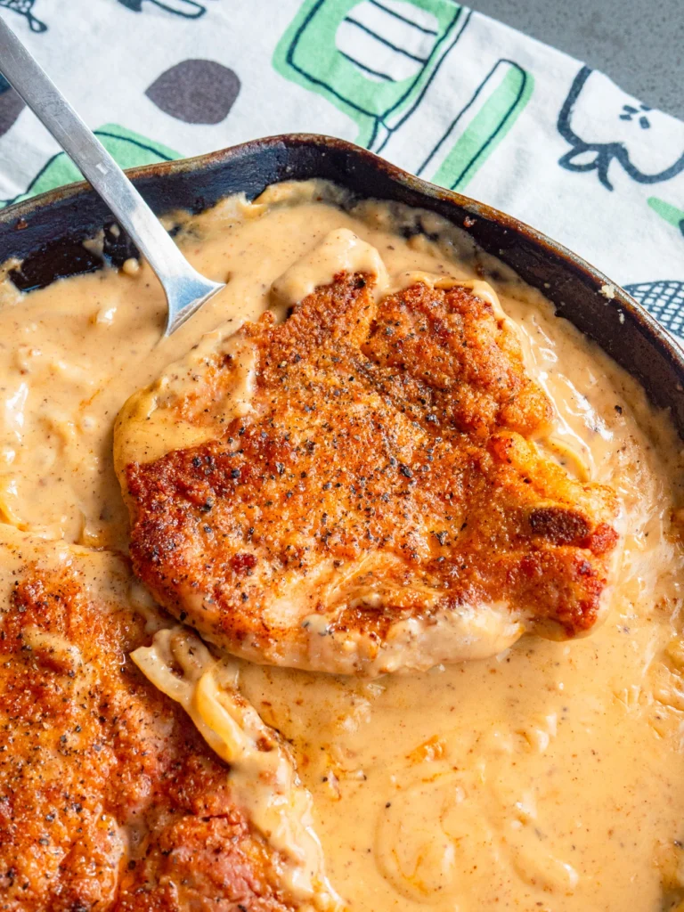 A close-up of Southern Smothered Pork Chops in a creamy gravy, cooked to golden brown perfection in a skillet.