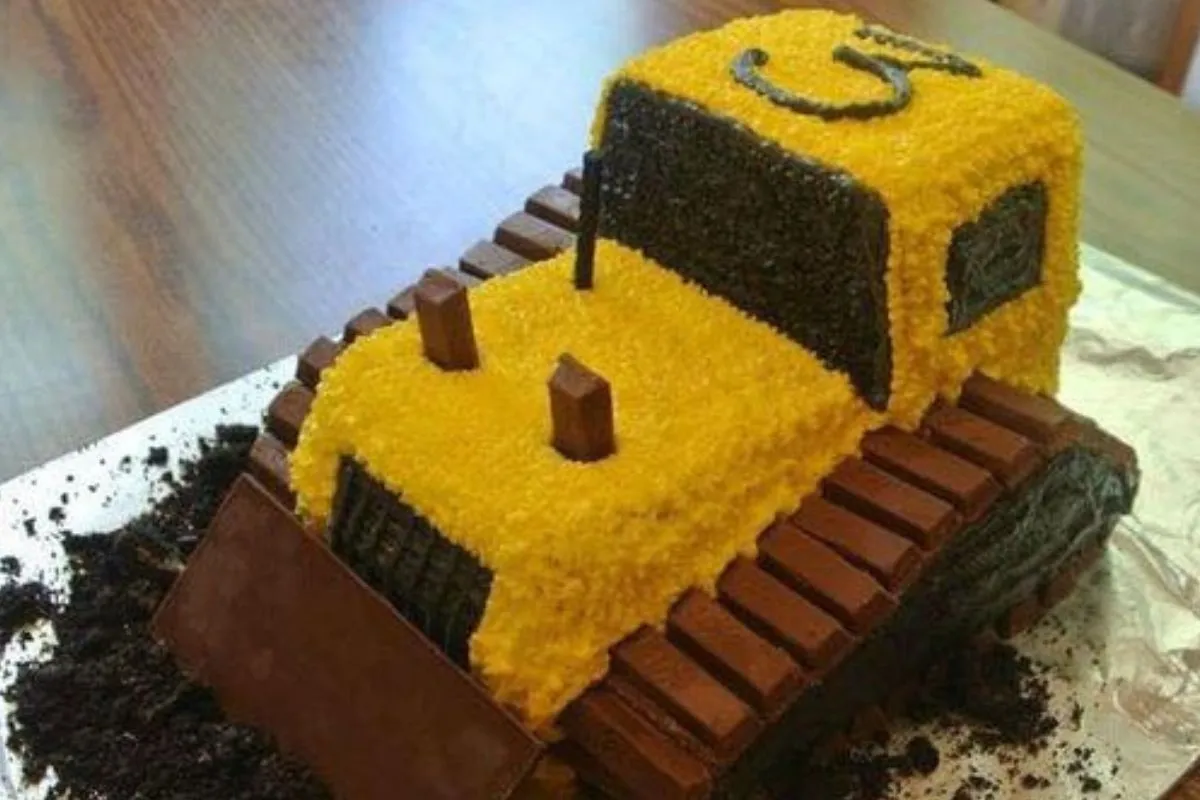 Yellow bulldozer cake made with Kit Kat bars and chocolate frosting on a dirt surface