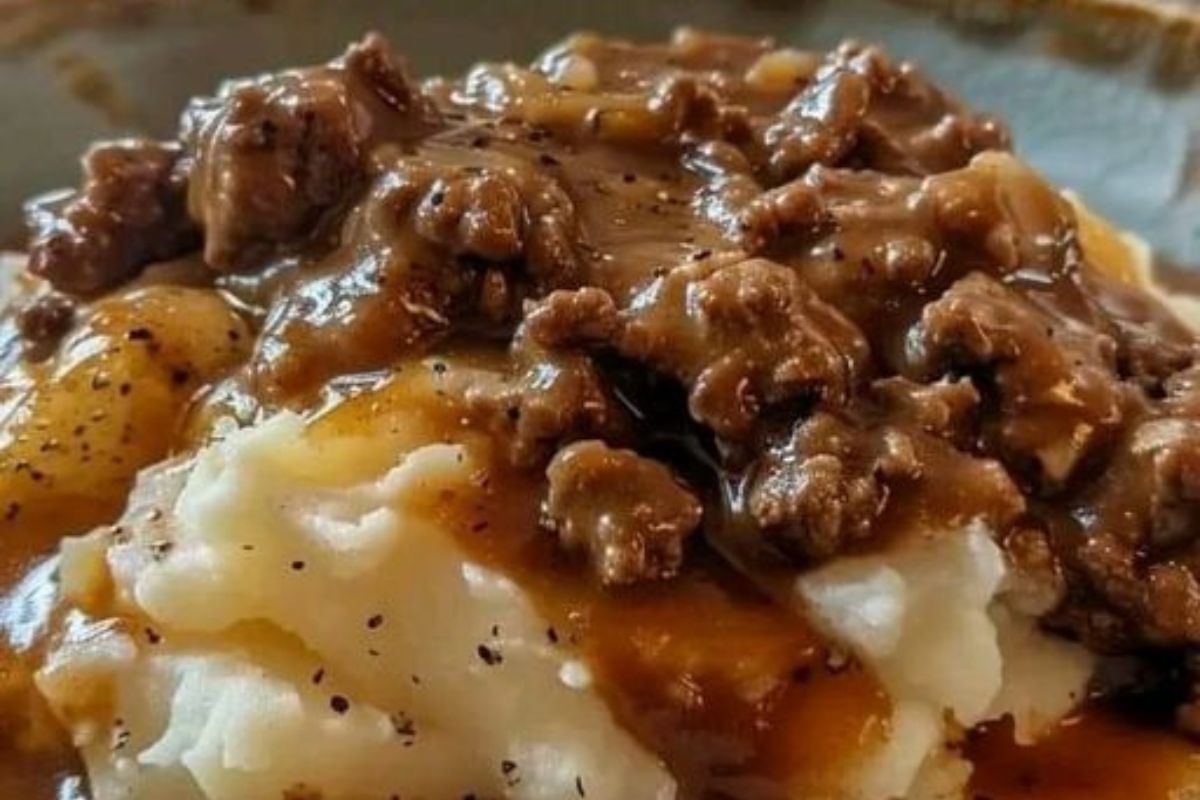 Close-up of savory ground beef gravy with chunks of meat poured over fluffy mashed potatoes on a rustic plate