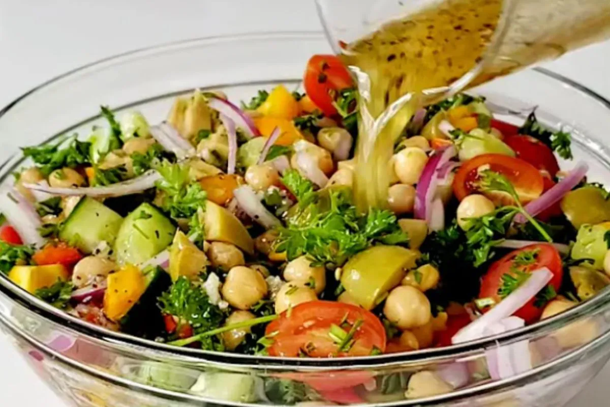 A colorful Mediterranean chickpea salad with diced cucumbers, cherry tomatoes, mixed bell peppers, olives, red onions, and parsley, dressed with a lemon and olive oil vinaigrette.