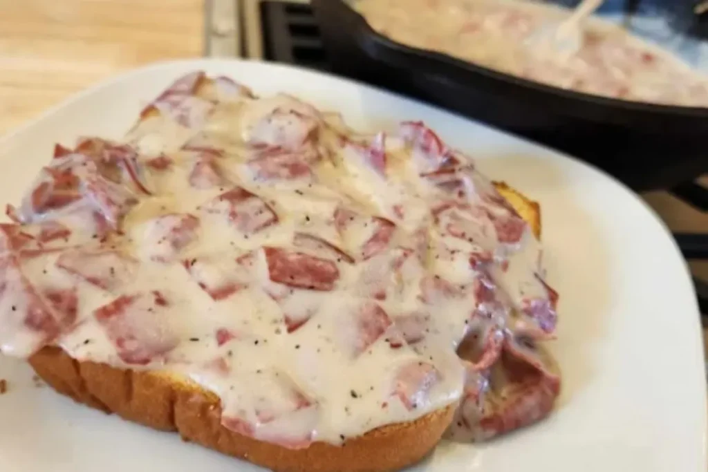 Creamy chipped beef gravy generously poured over golden toast, showing bits of pink beef in a rich white sauce