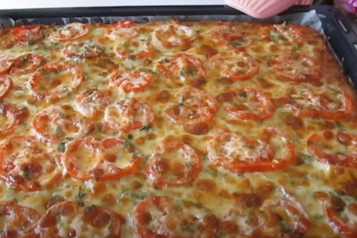 Freshly baked crispy potato cake topped with melted cheese and roasted tomato slices in a baking tray