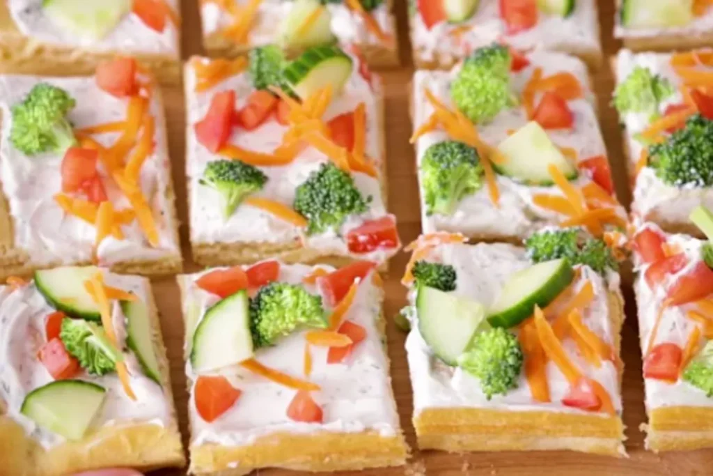 Slices of Easy Crescent Veggie Pizza topped with cream cheese, fresh vegetables, and shredded cheese