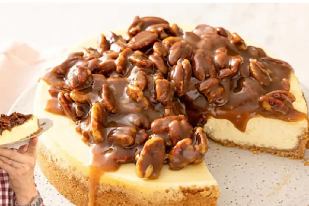 A slice of pecan pie cheesecake topped with caramelized pecans, showcasing a creamy cheesecake layer and a graham cracker crust