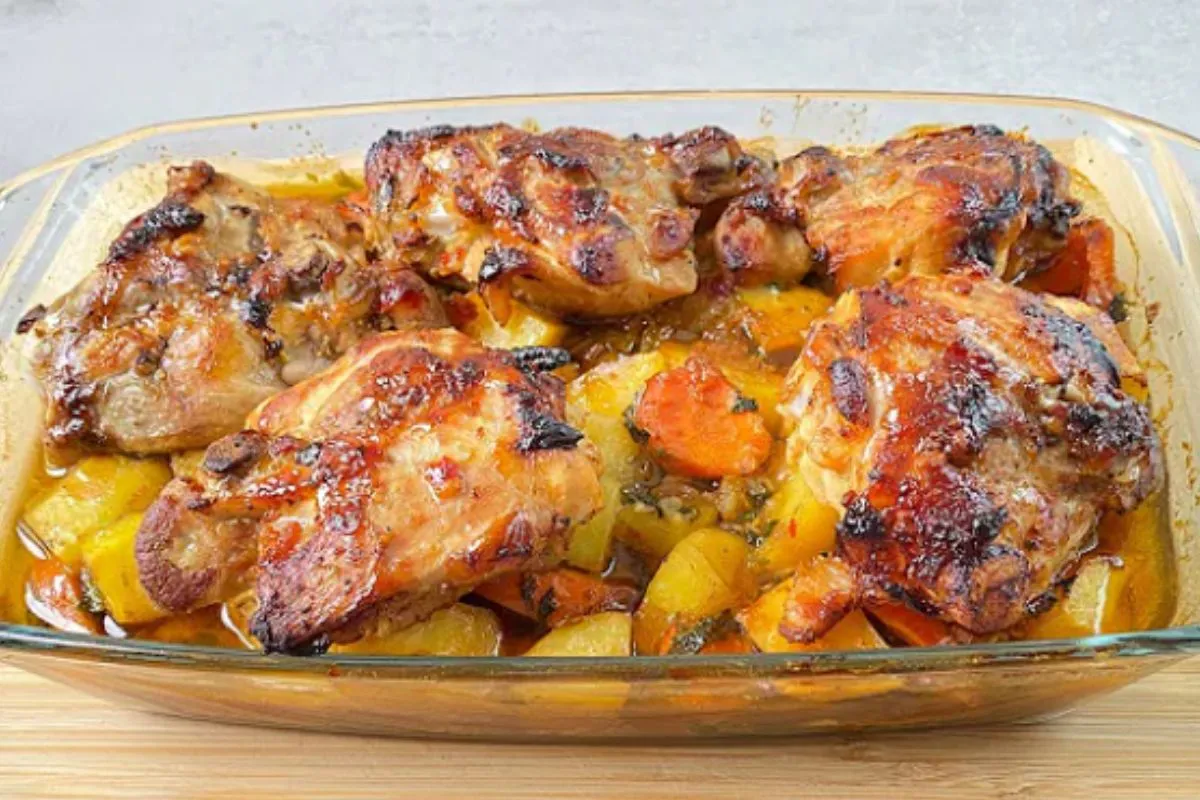 Golden brown chicken thighs with potatoes and carrots in a baking dish