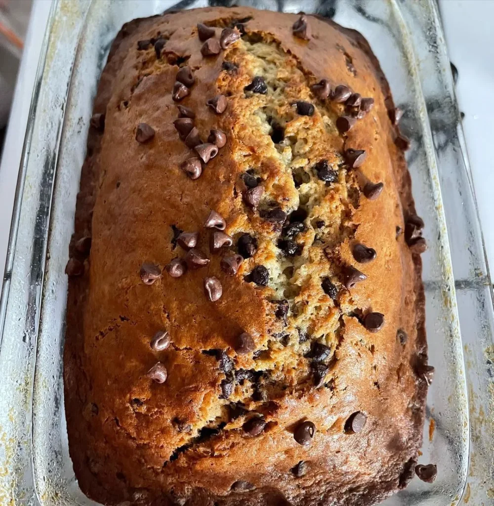 Freshly baked chocolate chip banana bread in a glass loaf pan, topped with chocolate chips