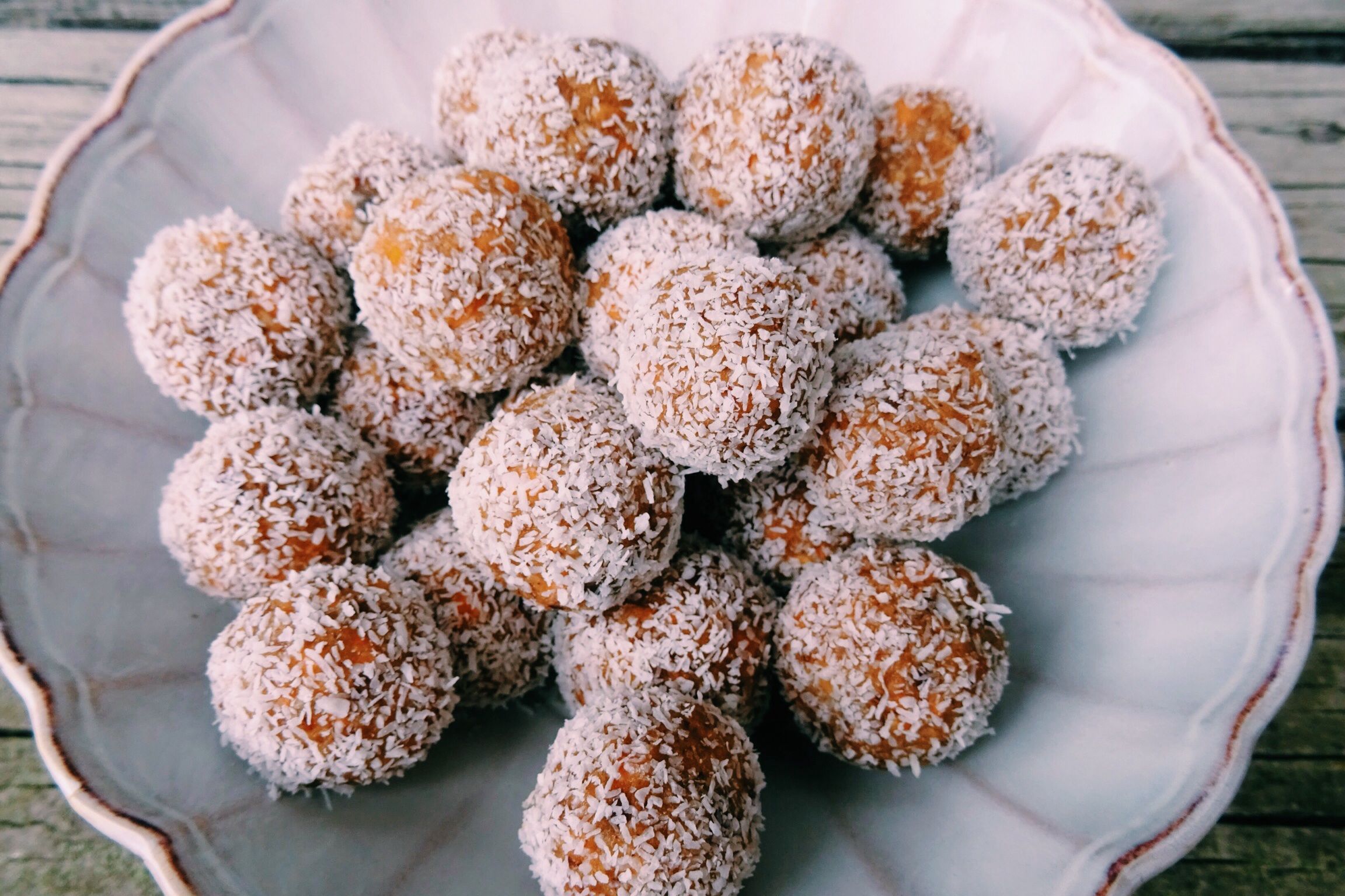 Homemade coconut-covered energy balls piled on a decorative white plate