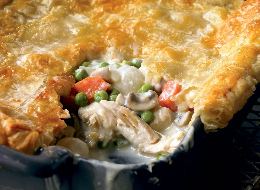 Close-up view of a slice of chicken pot pie with golden crust, filled with creamy chicken, carrots, peas, and mushrooms.