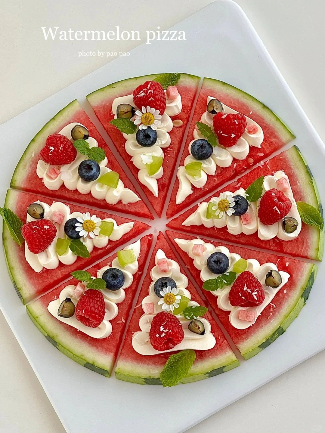 Watermelon pizza slices topped with fresh raspberries, blueberries, mint leaves, and cream on a white plate