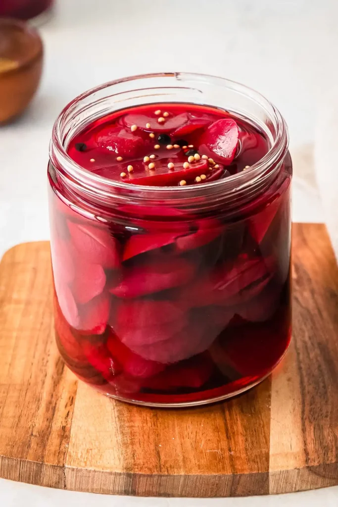 Jar of homemade pickled beets with mustard seeds on a wooden cutting board