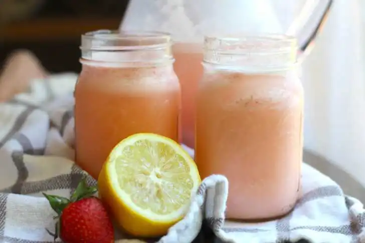 Two mason jars filled with pink strawberries and cream lemonade, garnished with a lemon slice and fresh strawberry